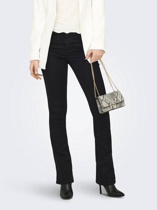 Model in zwarte flared jeans, witte blazer, met zilveren tasje en zwarte laarzen.
