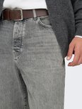 Detail van een grijze jeans met een bruine riem en een man die zijn hand in zijn zak steekt.