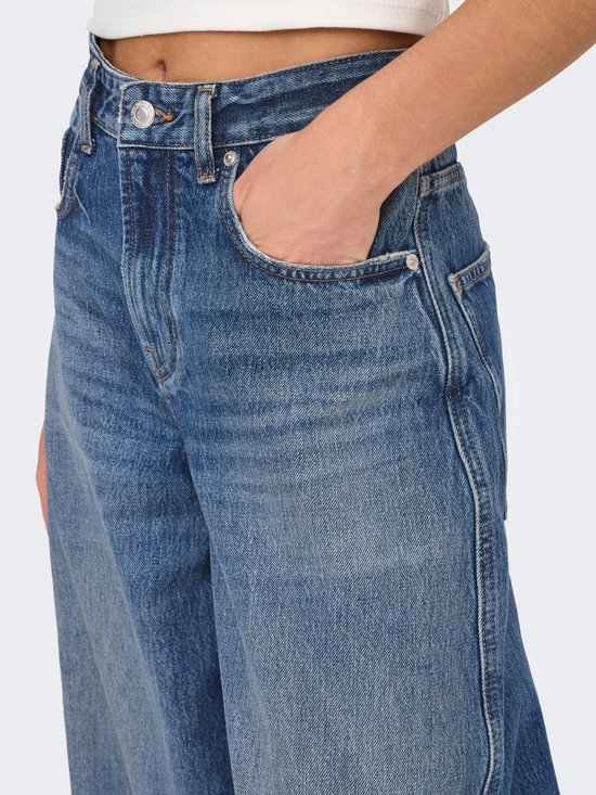 Close-up van een middendonkere, wijde spijkerbroek met hoge taille. Model steekt hand in de zak.