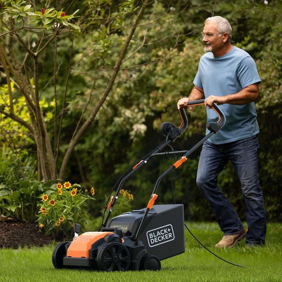 Man met bril duwt de zwarte en oranje BLACK+DECKER verticuteerder op het gras in een tuin.