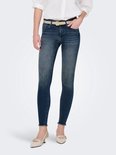 Model in witte blouse, beige riem en donkerblauwe skinny jeans met rafelige zoom.