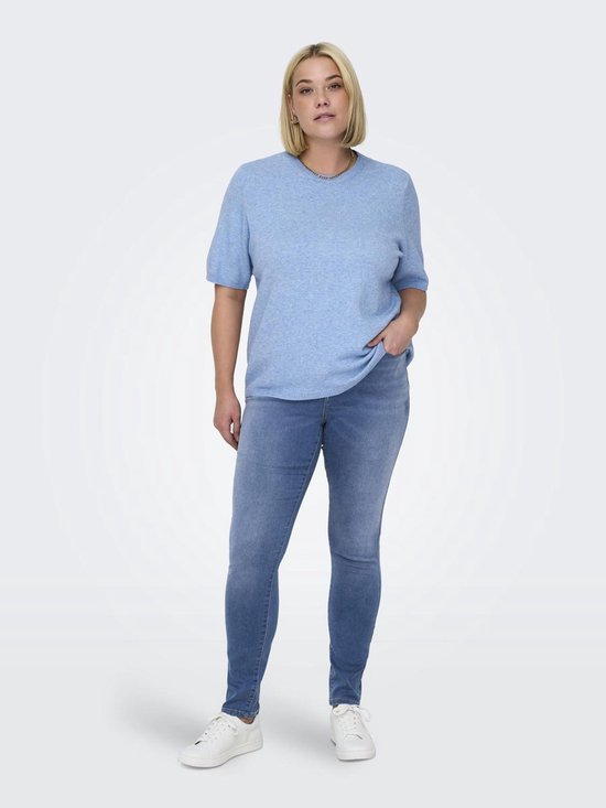 Model met blonde bob draagt blauwe skinny jeans en een lichtblauwe trui.