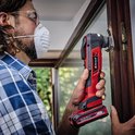 Man met rood-zwarte multitool werkt aan een houten raamkozijn.