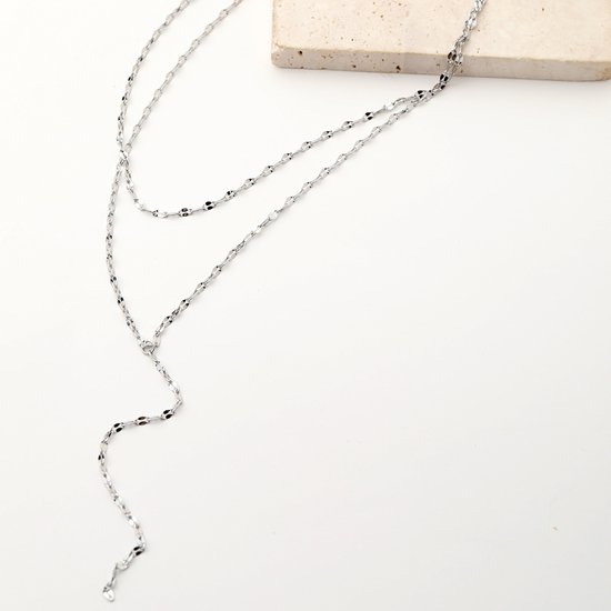 Close-up van een gelaagde zilverkleurige ketting met fijne schakels en een Y-vormige drop.