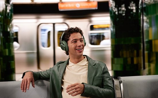 Man met groene koptelefoon lachend op een metrostation.