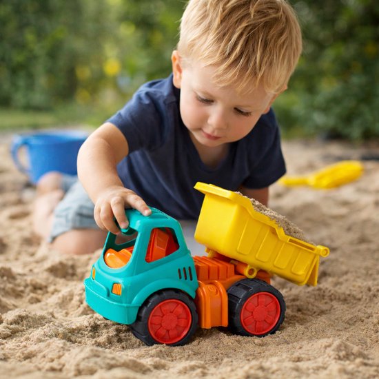Jongetje speelt met teal, oranje en gele kiepwagen gevuld met zand.