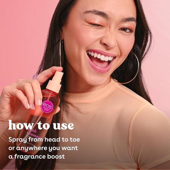 Vrouw met oranje oogschaduw houdt roze body mist van eos vast. Ze knipoogt en lacht.