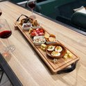 Houten serveerplank met hapjes, waaronder eieren, worstjes, olijven en kaasblokjes, op een houten tafel met wijnglazen.