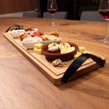 Houten serveerplank met diverse hapjes, waaronder eieren, worstjes, olijven en kaasblokjes, op een houten tafel met wijnglazen.