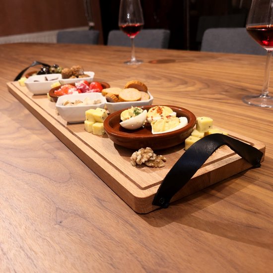 Houten serveerplank met diverse hapjes, waaronder eieren, worstjes, olijven en kaasblokjes, op een houten tafel met wijnglazen.