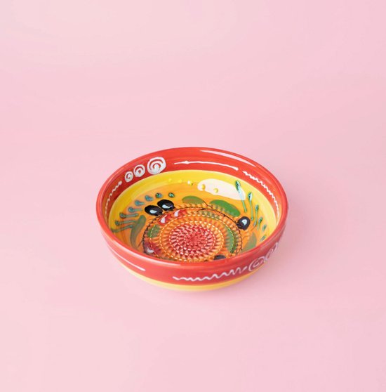 Une râpe en céramique avec un motif jaune, orange et rouge, décorée d'olives noires et de feuilles vertes.