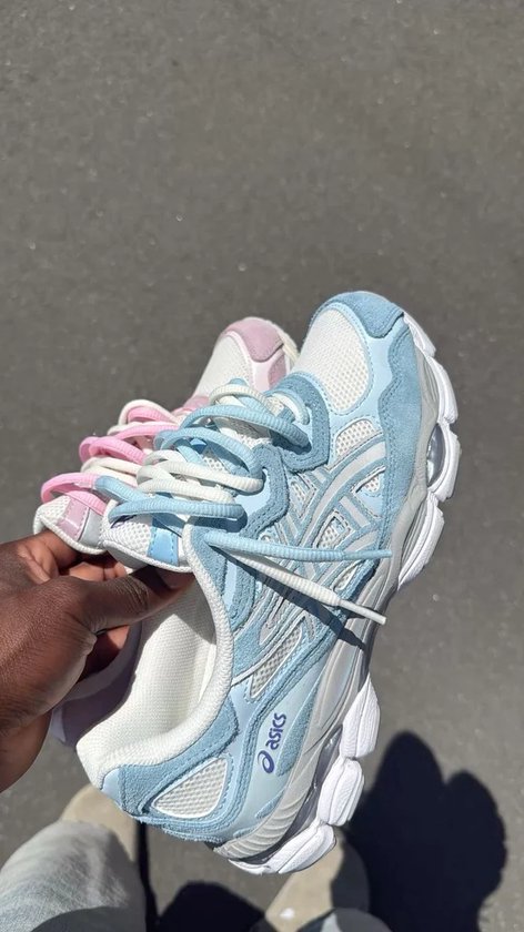 Hand die lichtblauwe en roze ASICS sneakers vasthoudt met witte veters.
