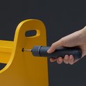 Hand gebruikt een donkerblauwe elektrische schroevendraaier om in een geel object te schroeven.
