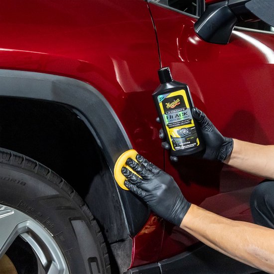 Hand in zwarte handschoen brengt Meguiar's Ultimate Black aan op zwarte kunststof wielkast van rode auto.