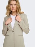 Beige blazer met één knoopsluiting, opgestikte zakken en omgeslagen revers. Model met blonde krullen, handen voor de borst.