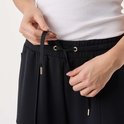 Detail van de tailleband van een zwarte joggingbroek met trekkoord en gouden oogjes.