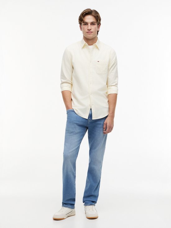 Man in lichtgele gestreepte blouse en blauwe jeans met lichte wassing.