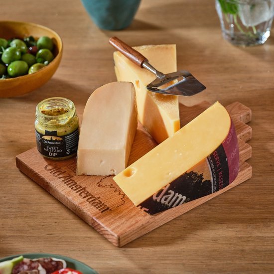 Houten plank met stukken kaas, mosterd, en olijven. Een kaasrasp ligt bovenop.