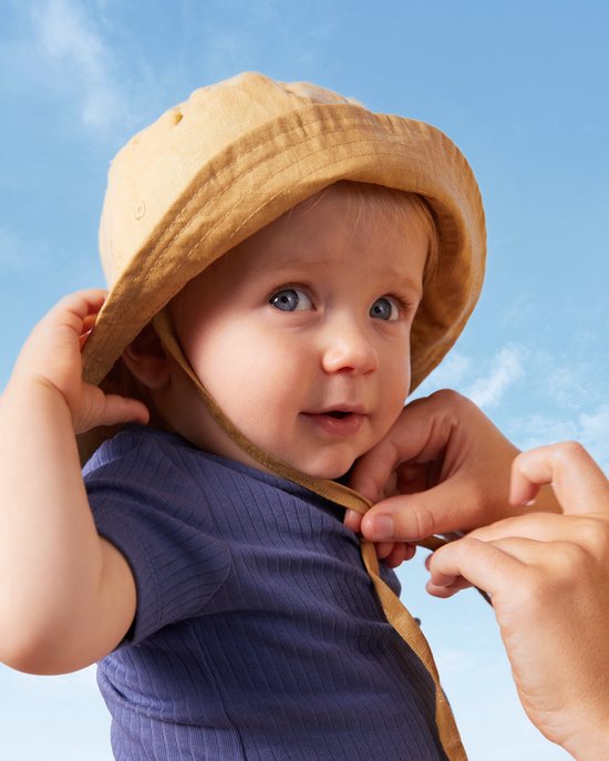 Een baby met blauwe ogen en een zonnehoed, die het strikje vastmaakt.