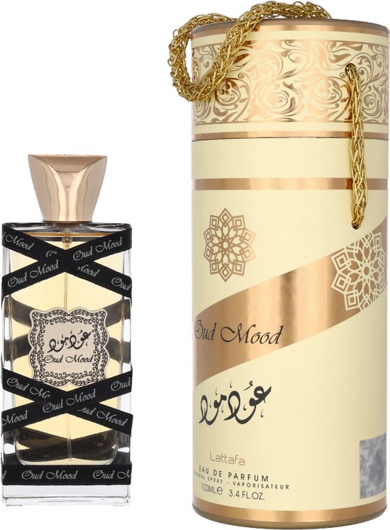 Oud Mood parfumfles met gouden dop, omwikkeld met zwart lint met "Oud Mood" erop, naast een bijpassende cilinderverpakking.