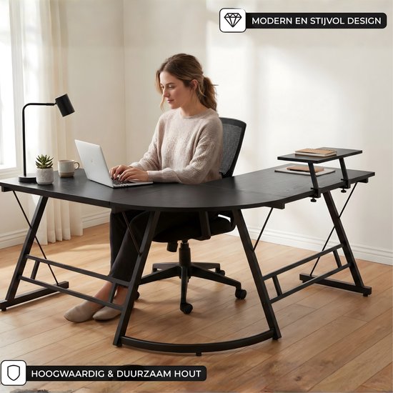 Vrouw aan een zwart L-vormig bureau met laptop, met een comfortabele bureaustoel en een plaid, in een lichte ruimte.
