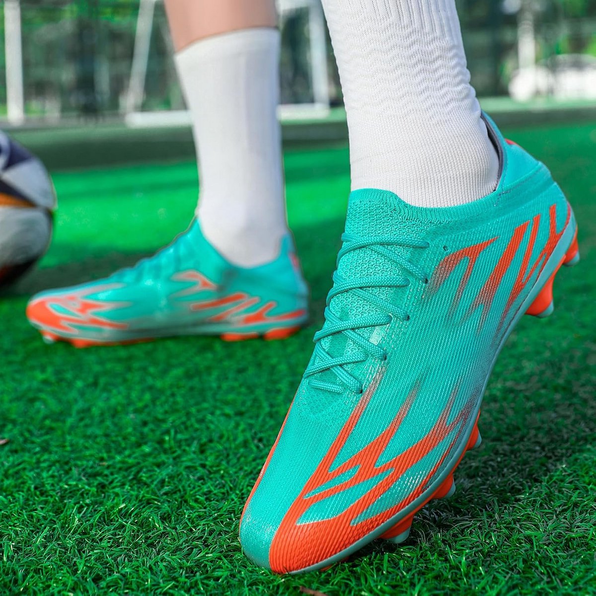Professionele heren voetbalschoenen in turquoise met oranje details, ontworpen voor grip en stabiliteit op gras.