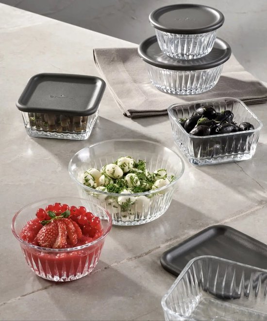 Bols en verre de différentes formes et tailles, remplis d'olives, de fraises, de groseilles et d'herbes.