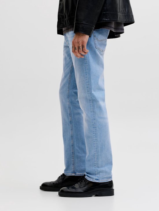 Zijaanzicht van een model in lichtblauwe slim fit jeans en zwarte schoenen.