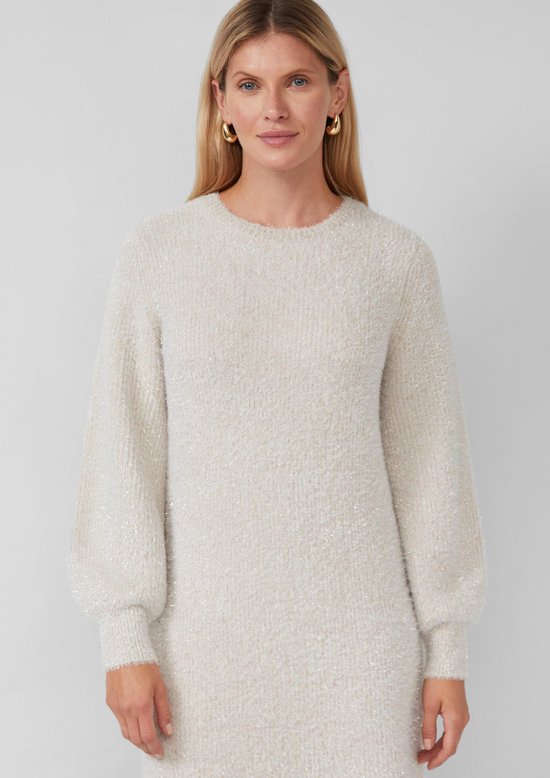 Close-up van een vrouw in een beige gebreide jurk met glitters en pofmouwen.