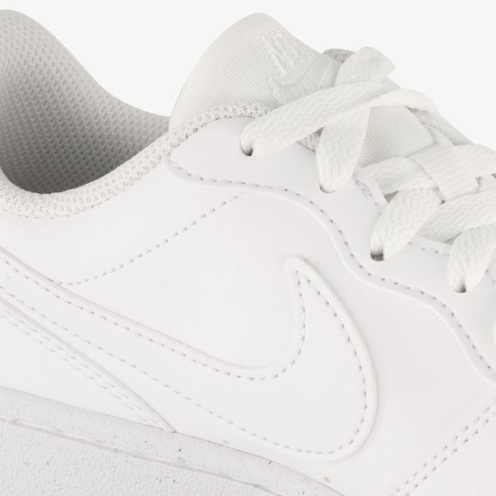 Detail van witte leren Nike sneakers: Nike logo op de tong en gespikkelde zool.