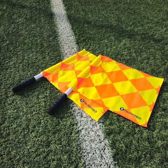 Twee grensrechtervlaggen met een ruitpatroon van geel en oranje, liggend op een voetbalveld met witte lijn.
