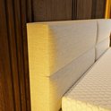 Een close-up van de hoek van het gestreepte beige hoofdbord van de boxspring, naast het matras.