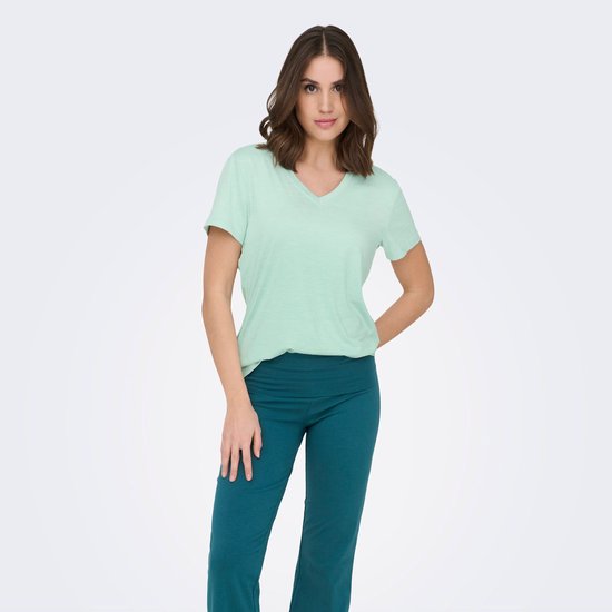 Model presenteert een lichtgroen V-hals t-shirt met korte mouwen en een turquoise broek.