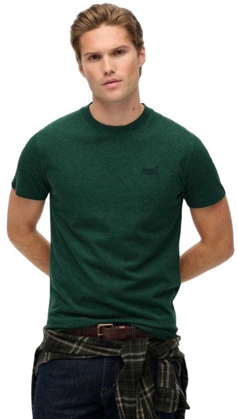 Homme portant un t-shirt Superdry vert foncé et un jean, mains derrière le dos.