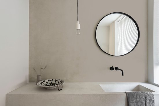 Badkamer met een betonnen wastafel, ronde spiegel met zwart frame en zwarte kraan.