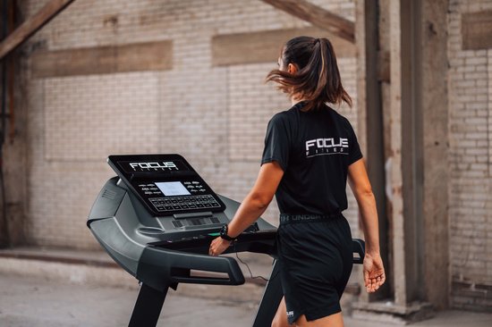 Vrouw met paardenstaart in zwart Focus Fitness shirt en zwarte broek loopt op een loopband.