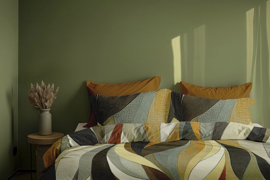Lit avec couette à motif ondulé dans des tons terreux, orange et vert. Deux oreillers orange.