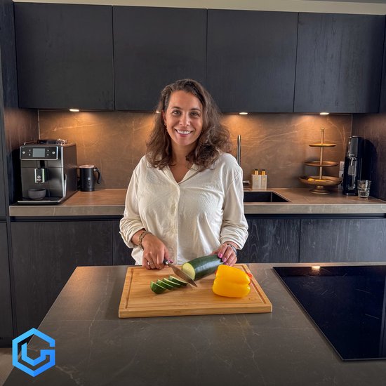 Vrouw snijdt komkommer en gele paprika op een bamboe snijplank in een moderne keuken.