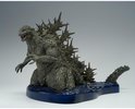 Grijze Godzilla figuur met scherpe rugplaten, op een blauwe waterbasis.