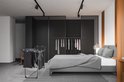 Antraciet droogrek met kleding in een slaapkamer, naast een bed met grijze deken.
