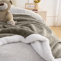 Taupe fleece plaid met witte sherpavoring, met een teddybeer en decoratieve kalender op de achtergrond.