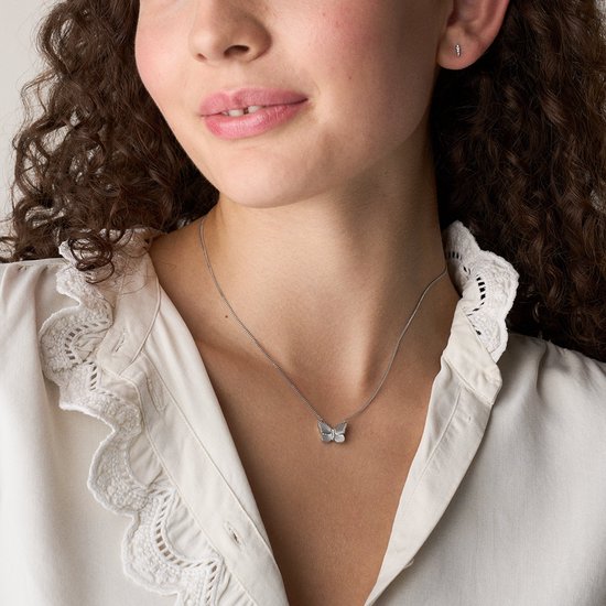 Model draagt een zilverkleurig collier met een vlinderhanger op een wit shirt.