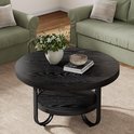 Zwarte ronde salontafel met een opbergplank, met een vaas bloemen en een decoratieve kom bovenop.