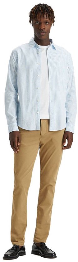 Man in een gestreepte lichtblauwe blouse, wit T-shirt en beige chino broek.