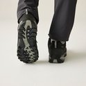 Achterkant van zwarte wandelschoenen met grijze zolen, gedragen door een persoon in een grijze broek.