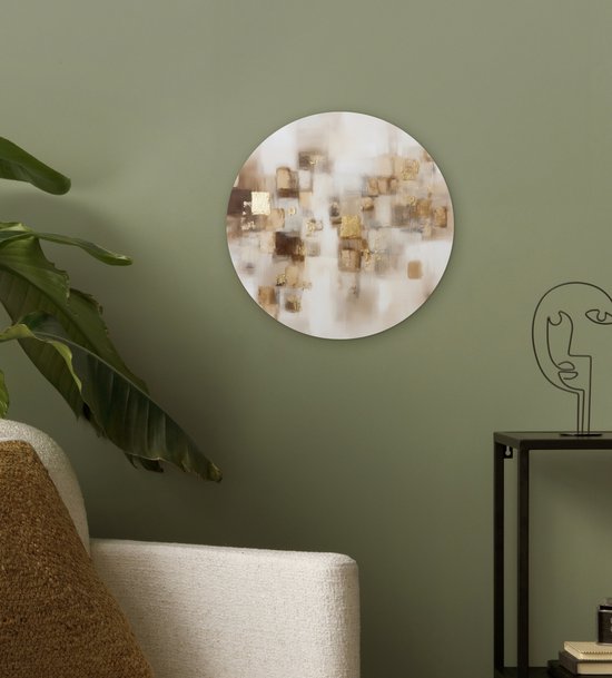 Ronde muurdecoratie met abstracte gouden en bruine vierkanten hangt aan een groene muur boven een witte bank.