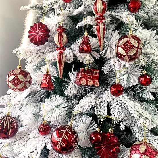 Rode kerstballen met gouden glitter en bordeaux accenten op een met sneeuw bedekte kerstboom.