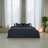 Een slaapkamer met een opgemaakt bed met donkerblauw dekbedovertrek en kussenslopen.