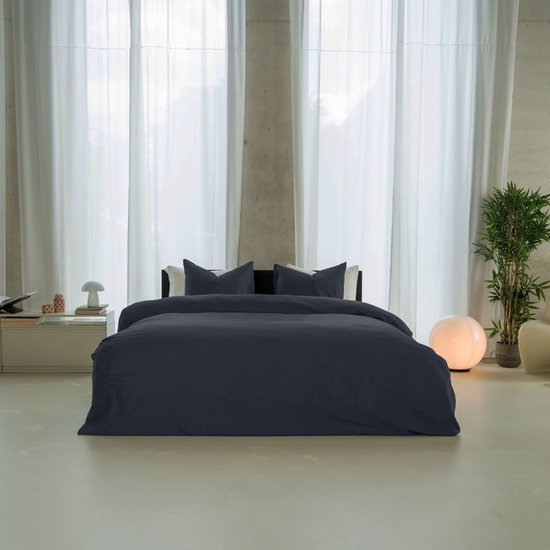 Een slaapkamer met een opgemaakt bed met donkerblauw dekbedovertrek en kussenslopen.