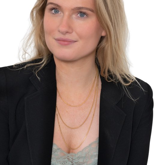 Model met blond haar draagt drie gouden kettingen.
